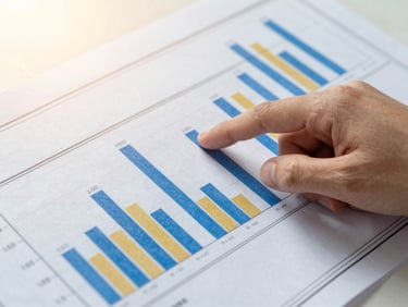 Close-up of a hand pointing to figures on a financial report with a blueprint overlay, bright clean morning light, rich royal blue and gold accents