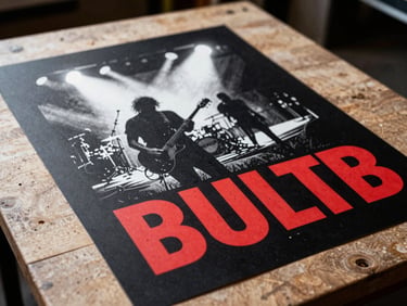 Hand-pulled screenprinted gig poster with bold red and white typography on black paper, lying on a wooden workshop table, dramatic backlighting