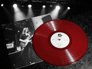 A thick red vinyl record resting on its printed gatefold sleeve, high-contrast stage lighting reflecting off the grooves, 35mm film grain