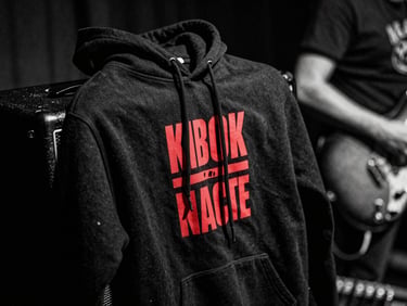 Gritty close-up of a black cotton hoodie with a bold red screenprinted graphic, draped over a guitar amplifier, dramatic side lighting