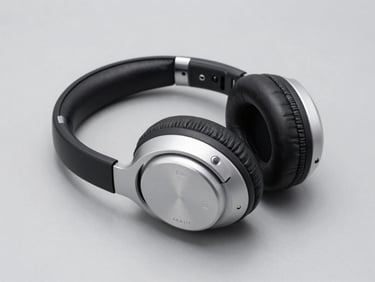 3/4 angle studio photograph of over-ear wireless headphones, black and silver colorway, folded flat on a neutral grey surface, bright diffused studio lighting