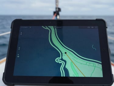 Macro close-up of a rugged Android tablet screen showing a high-contrast marine navigation chart with seafoam green vector lines, mounted on a sailboat cockpit under overcast daylight.