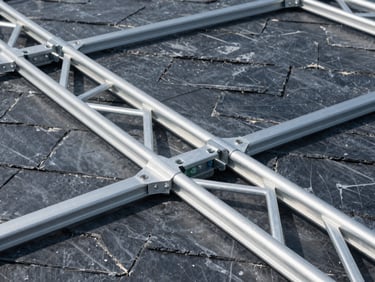 Geometric close-up of heavy aluminum truss joints being secured in an exhibition pavilion, industrial slate background, sharp focus.