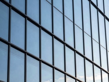 Architectural detail of a modern glass facade reflecting a bright blue sky, sharp geometric lines, high-contrast natural daylight showing zero residue.