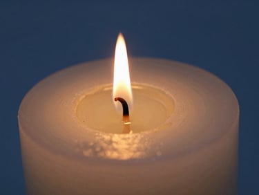 Macro shot of a burning candle wick, warm golden flame casting light on a pooling clear oil, deep blue background, shallow depth of field.