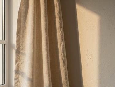 Detail of raw linen drapery catching soft golden-hour light next to a textured plaster wall, warm neutral tones