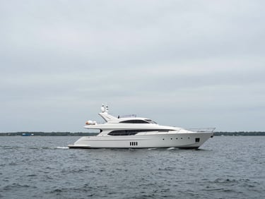 Wide environmental shot of a ninety-foot flybridge motor yacht underway on Narragansett Bay, overcast silver-grey maritime day, low horizon, negative space in sky