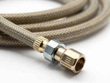 Macro close-up of a coiled high-pressure LPG gas hose with metal end fittings and a steel clamp, shot against a plain white background under studio strobe, sharp focus on the hose braid texture and clamp teeth