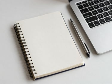 Overhead close-up of a blank notebook opened to the first page beside a laptop keyboard on a clean white desk, single pen placed diagonally, even natural daylight from the left