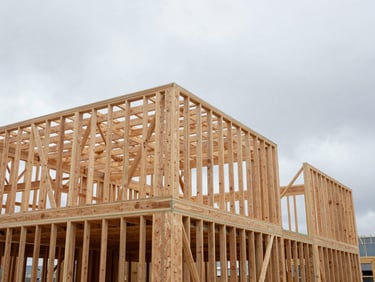 Overcast daylight wide-angle shot of a modern timber-framed building under construction, raw wooden beams visible against a neutral sky, clean technical lines.