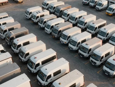 Wide-angle overhead shot of a commercial fleet yard at daylight — rows of trucks and vans parked in formation, asphalt lot, no people, operational scale evident