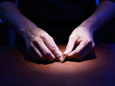 Close-up of hands working with raw leather under a focused spotlight, dark moody background, high contrast, 35mm