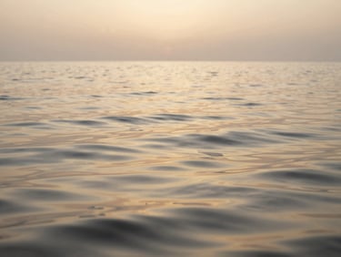 Calm water ripples reflecting a soft golden sunset sky, serene natural texture