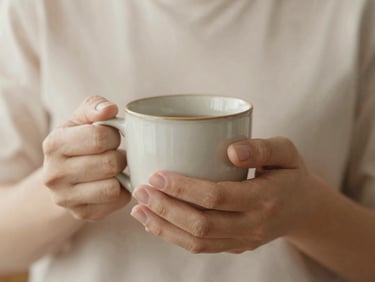 Soft focus on two hands holding a warm ceramic mug, diffused morning light, peaceful and supportive feeling