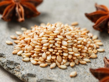 Macro close-up of raw golden sesame seeds and whole spices on a neutral stone slab, crisp natural morning light, sharp focus on textures.