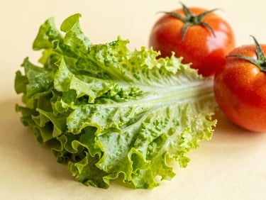 Vibrant fresh green lettuce leaves and ripe red tomatoes on a light pastel yellow background, natural morning light, close-up