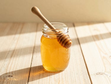 A glass jar of thick golden honey with a wooden dipper, sun-drenched rustic table, warm orange tones