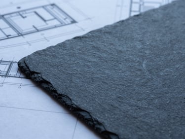 Tight macro crop of analytical materials and architectural blueprints on a dark slate table, cool overcast daylight, minimalist editorial style