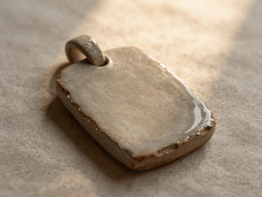 Close-up of a unique stoneware pendant with a raw clay edge, resting on textured linen, warm diffused light, rich earthy tones.