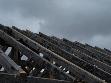 Low-angle view of timber roof rafters under construction, dark moody sky background, sharp architectural lines