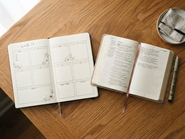 Overhead flat-lay of a printed journaling layout resting on a warm wooden desk beside an open Bible, soft morning window light, gentle shadows.