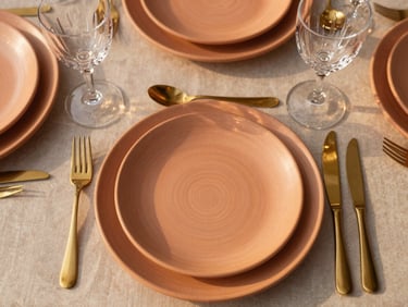 Overhead flatlay of a luxury table setting with textured terracotta plates, gold cutlery, and crystal glasses, warm natural golden-hour light