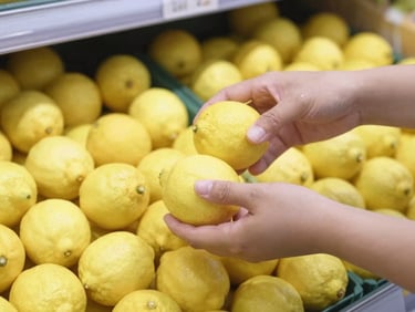Close-up of hands picking loose fresh lemons in a bright grocery store, natural daylight, focus on sustainable packaging