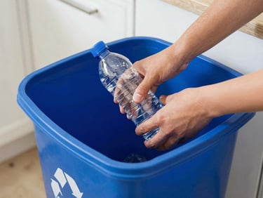Hands placing a clean plastic bottle into a blue recycling bin in a bright California kitchen, natural daylight