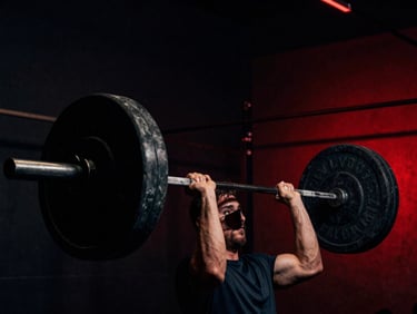 Moody athletic photography of hands gripping a heavily loaded barbell in a dark gym, high-contrast low-key lighting, dramatic red ambient backlight, 35mm film.