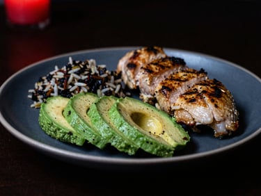 Moody close-up shot of a clean, macro-balanced meal with sliced avocado, grilled chicken, and wild rice under dramatic low-key lighting, 35mm film