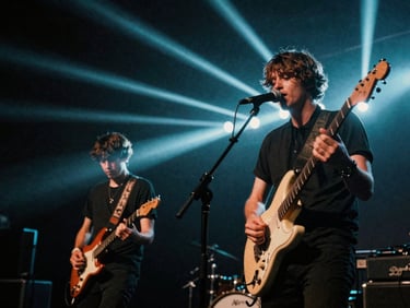 Dynamic low-angle shot of two musicians performing on a dimly lit stage with intense strobe lights.