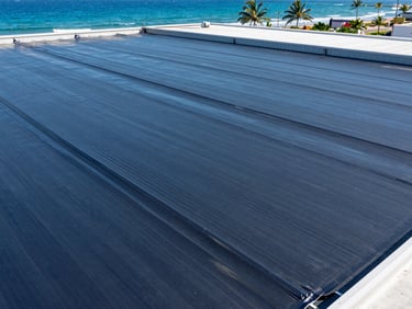High-angle crisp architectural shot of heavy-duty waterproofing membranes heat-sealed on a massive port warehouse roof, bright coastal daylight