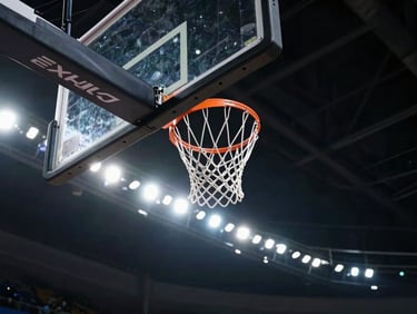 Dramatic low-angle shot of a basketball hoop against a dark stadium ceiling, bright floodlights creating a halo effect, high contrast.