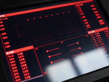 Extreme close-up overhead shot of a tactical operations dashboard interface, deep black background with crimson red data streams and glowing status indicators, multiple metric panels showing live throughput numbers, circuit-board grid lines faintly visible beneath the glass surface, cinematic backlight from below casting sharp shadows upward