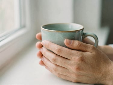 Close up of gentle hands holding a warm ceramic mug, soft morning light, peaceful domestic setting, shallow depth of field