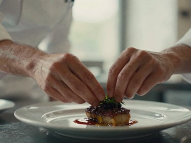 A close-up shot of a chef's hands meticulously garnishing a dish in a warm Scandinavian-style restaurant kitchen, soft natural daylight, shallow depth of field, rich crimson and muted green tones, 35mm film style.