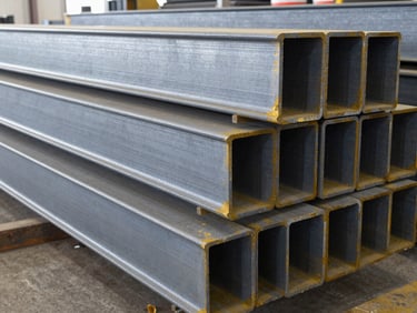 Stacks of heavy structural steel beams in a clean, organized warehouse under bright industrial lighting, cool steel tones, high detail.