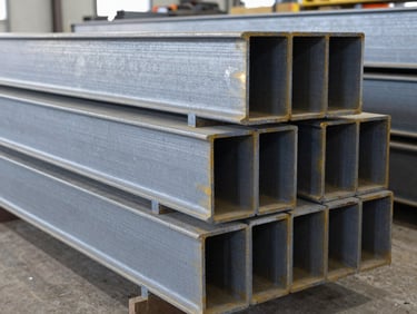 Stacks of heavy structural steel beams in a clean, organized warehouse under bright industrial lighting, cool steel tones, high detail.