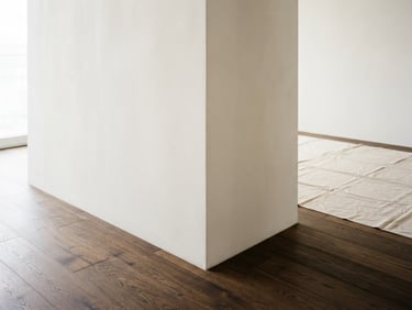 Straight-on architectural detail of a flawless plaster wall corner meeting a dark wooden floor, soft natural side-light, clean drop cloth in the background, 35mm lens