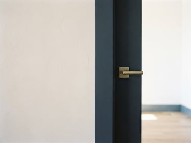 Straight-on architectural photograph of a pristine, sunlit residential room, focused on a razor-sharp paint edge where a neutral plaster wall meets a dark slate-navy trim, crisp details, 35mm lens