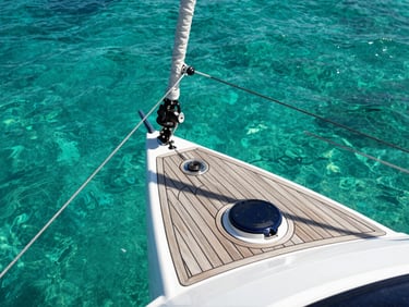 Close-up of high-end catamaran rigging and teak deck, crystal clear turquoise ocean water visible below, bright tropical sun casting sharp shadows.