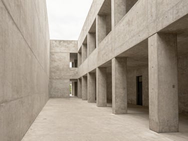 One-point perspective of an institutional concrete hallway, light-filled volumes, minimal architectural design.