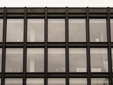 Exterior detail of a blackened steel and glass commercial office facade, straight-on elevation, desaturated warm neutral tones