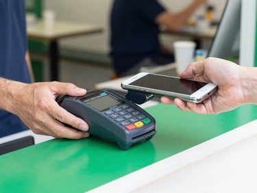 Close-up of a mobile card reader attached to a smartphone being handed across a cafe counter, bright daylight, clear focus on the transaction.
