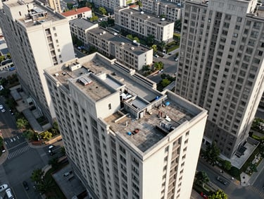 Overhead aerial framing of a mid-rise urban residential building rooftop and surrounding block grid, flat daylight, no people, street context visible below