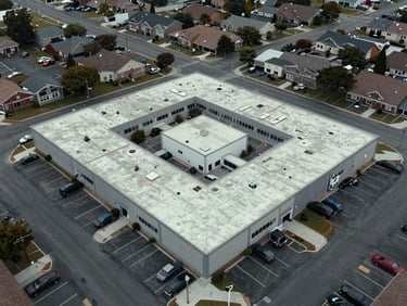 Overhead aerial framing of a suburban commercial block, flat-lit overcast daylight, rooftops and parking lot geometry visible, no people, site analysis framing