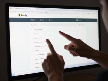 Close-up of hands pointing at a Shopify admin orders screen on a large monitor, studio tungsten lighting, dark background