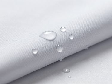 Macro shot of water droplets rolling off a treated technical fabric, bright cool-toned studio light, razor-sharp focus.