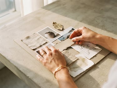 Close-up of hands arranging physical paper moodboard on a light concrete table, warm afternoon shadows, 35mm film grain