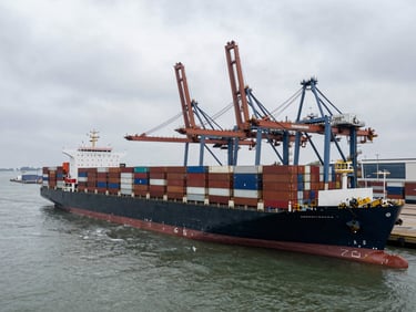 Wide-angle aerial shot of a massive container vessel docking at a modern deep-water port, overcast sky, industrial steel tones.